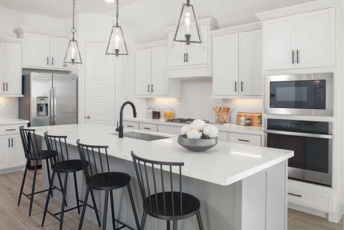 Kitchen with white cabinets and center island with built-in seating has three pendant lights