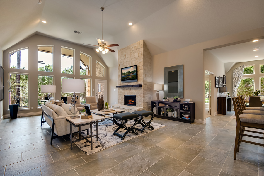 open-concept family room with stone fireplace, wall of windows, vaulted ceiling, grey tile floor and neutral décor