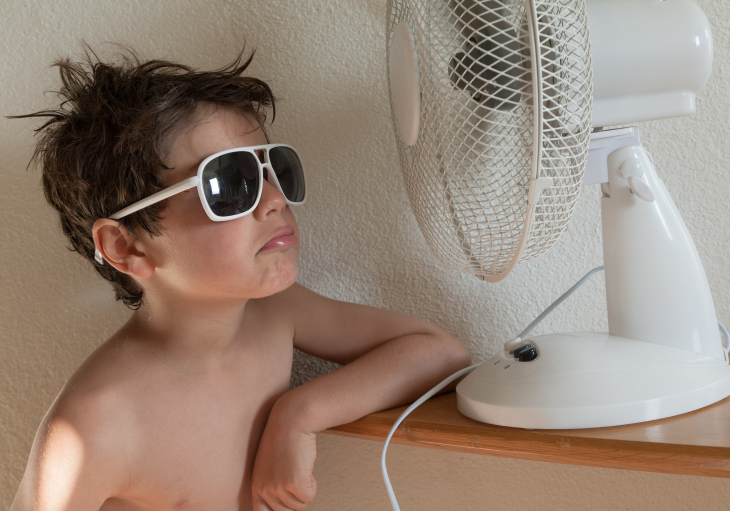 kid in sun glasses sitting by a fan to keep cool during the summer month