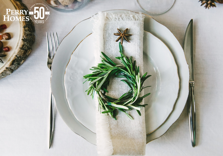 place setting on white tablecloth of white china dishes with gold edges topped with white napkin and simple green wreath