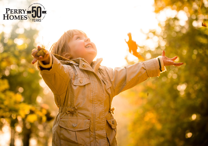 small child wearing a fall coat looking up with arms extended as if just threw leaves in the air