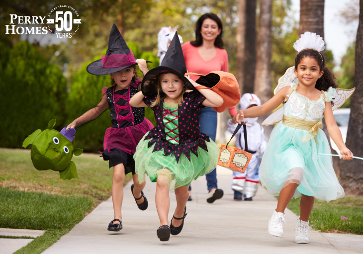 children in halloween costumes running down a sidewalk while adult walks behind them