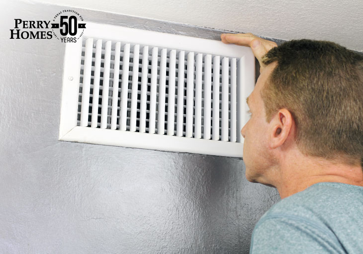 man inspects white residential air circulation wall vent that is on a grey painted wall just below a white ceiling 