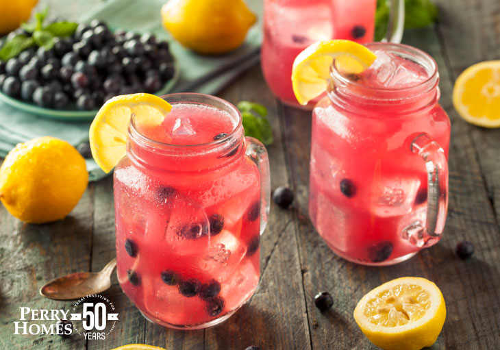 two mason jar glasses full with pink drink, blueberries, garnished with lemons sit on wood slatted table with lemons