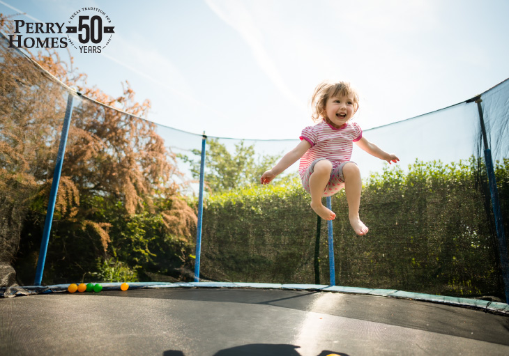 young girl approximately five years old jumping midair on trampoline with safety net enclosure walls with clear blue sky