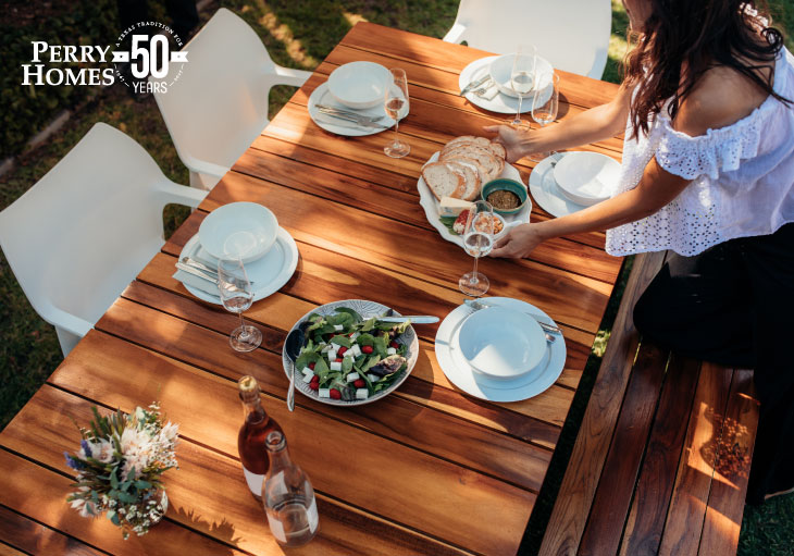 wooden picnic table with white chairs, plates, bowls and a salad