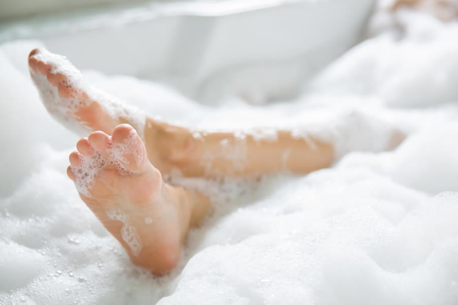 bottoms of two bare feet surrounded by white bubbles in bath