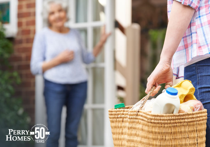 woman bringing woven bag full of groceries to elderly woman waiting at the door to receive them