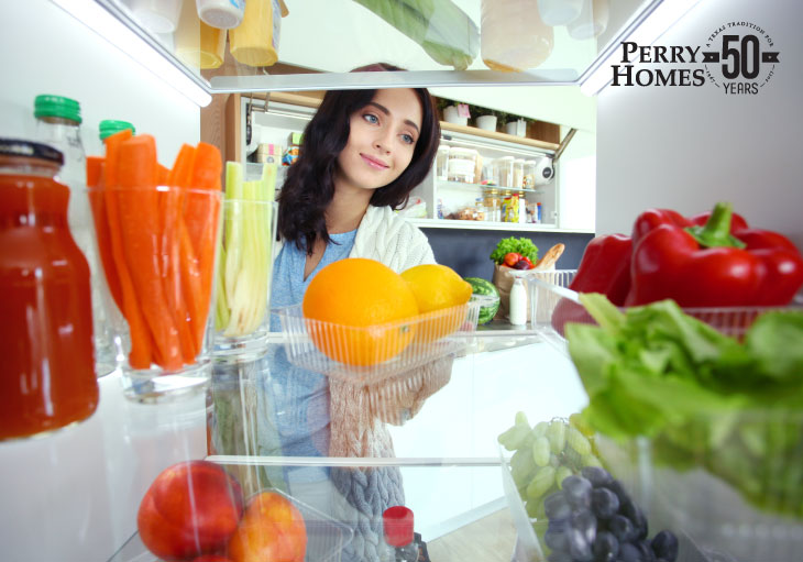 woman with long dark hair views inside of refrigerator that has fresh produce and juice on glass shelves