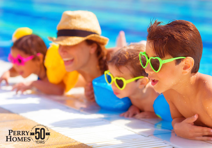three children with brightly colored sunglasses and woman with straw fedora hat in a swimming pool leaning up over the edge