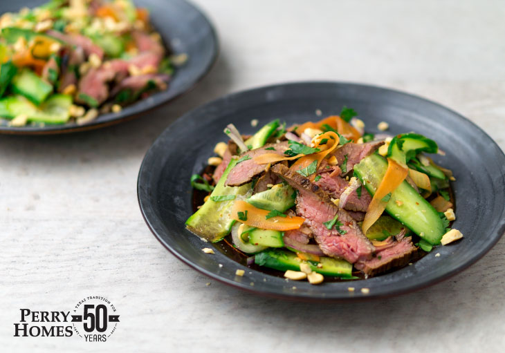 black plate holds slices of medium steak mixed with carrots and cucumbers and sprinkled with peanut pieces