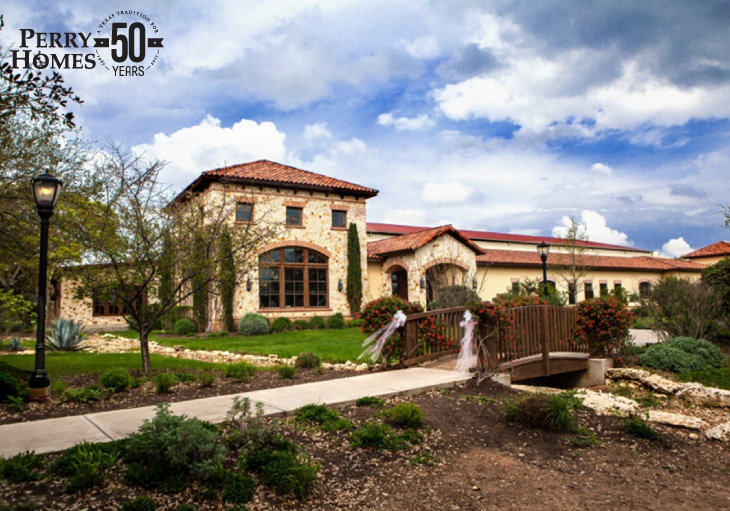building with spanish style roof, stucco and stone exterior and lush landscaping with arched bridge over a creek