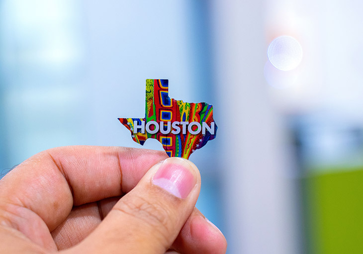 man's fingers holding texas shaped metal piece with bright colors and houston name