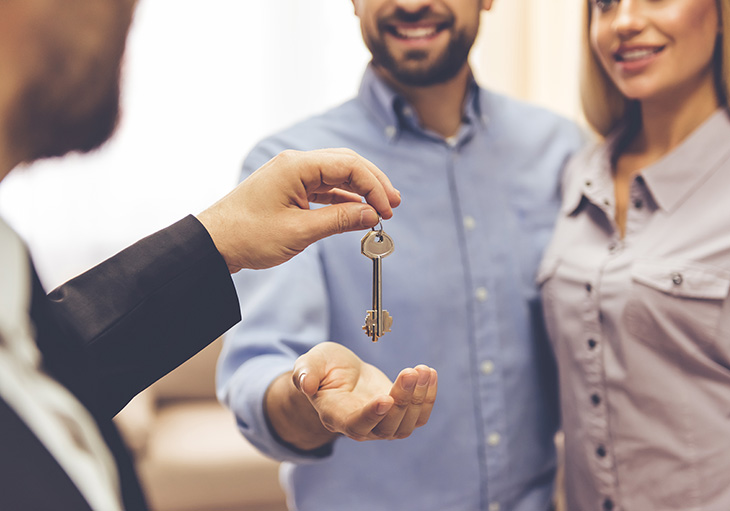 A man holds out his hand and accepts keys from a real estate agent to complete the last step in the home buying process.