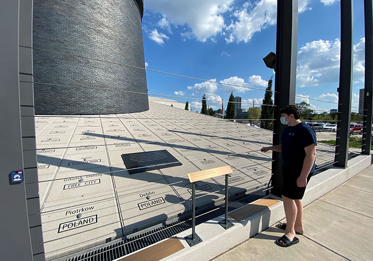 Young man stands looking at holocaust monument.