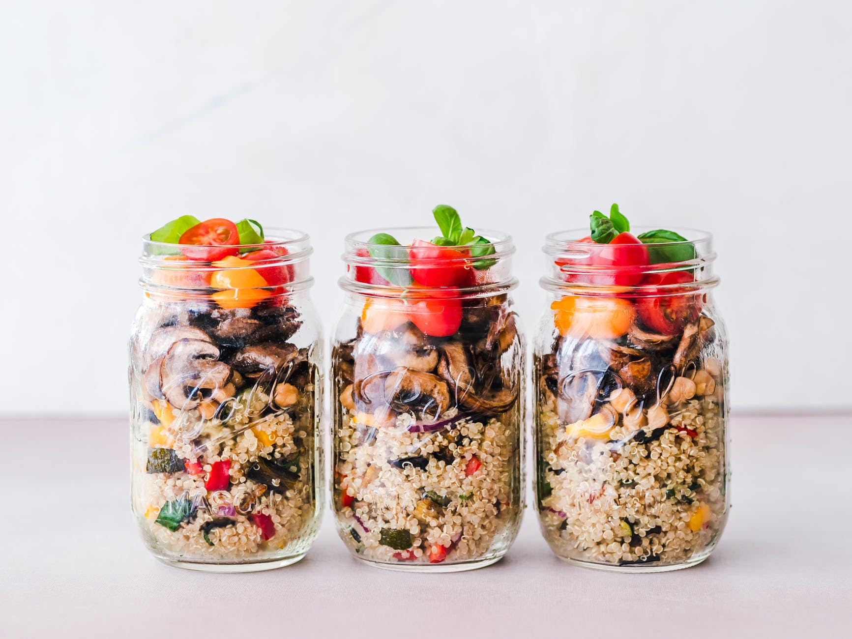three glass canning jars filled with a mix of quinoa, peppers, mushrooms, tomatoes and herbs