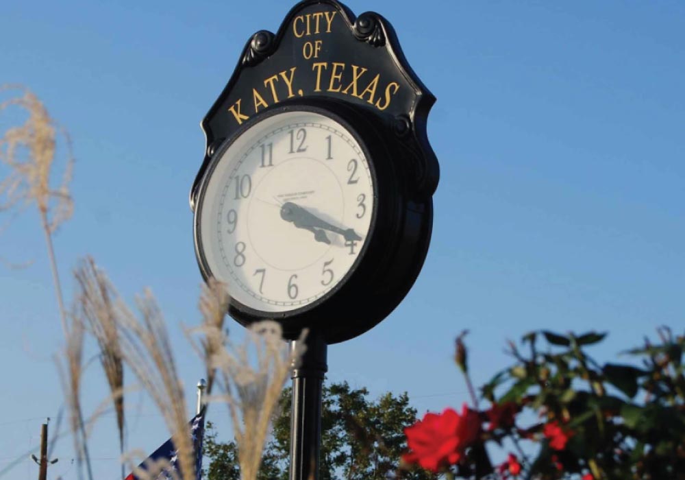 old-fashioned black street clock sign with the title city of katy texas painted at the top with a clear blue sky