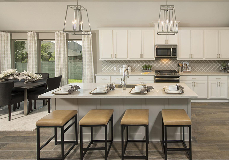 A beautifully designed kitchen features a large island and four brown leather bar stools.
