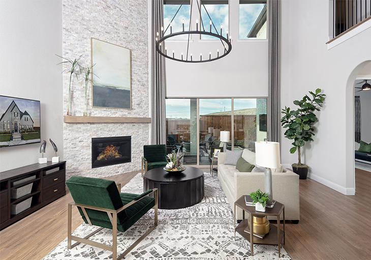 A modern living room with a couch and two green accent chairs next to a tall stone fireplace.