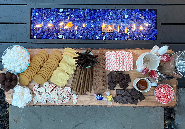 Tray filled with chocolates, candies and cookies sit besides a tabletop fire centerpiece.