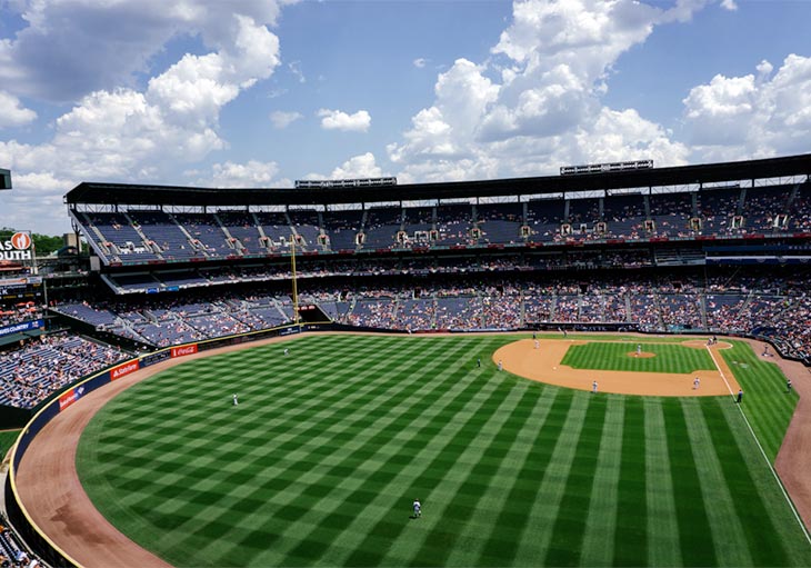 high level view of baseball field with blue sky and clouds and partially filled stadium with blue seats