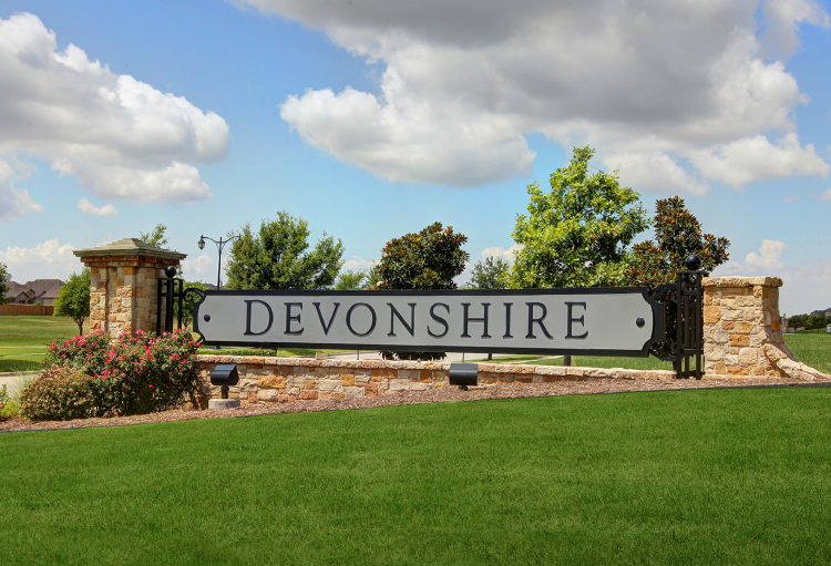 Green trees, lush grass and blue skies surround the entry sign for the Devonshire community in Dallas.