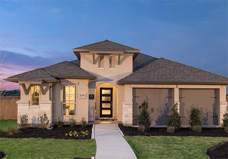 one story home with beige stucco and stone exterior, low-pitched roof at dusk