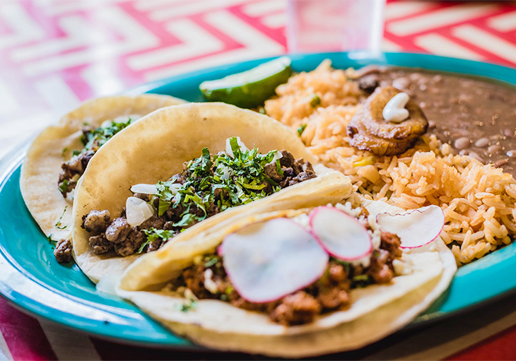 Three breakfast tacos in Austin sit on a blue plate with rice and refried beans.