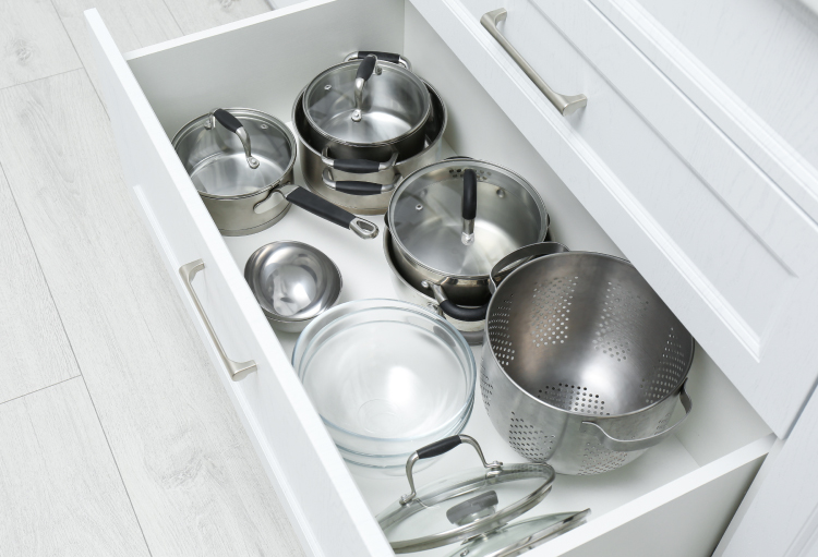 A series of stainless-steel cookware sits in an all-white kitchen drawer.