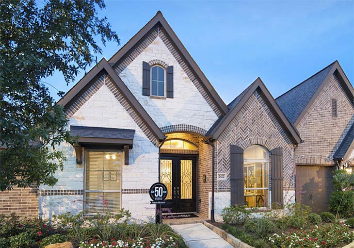 A Perry Homes move-in ready home featuring the 3465W design's mixture of white square bricks and herringbone red bricks lined by a lush garden and trees.