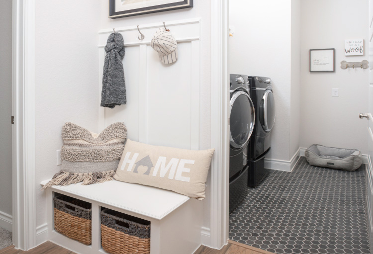 A clean and bright mudroom sits adjacent to a laundry room with hanging hats, scarves and a collection of white pillows.