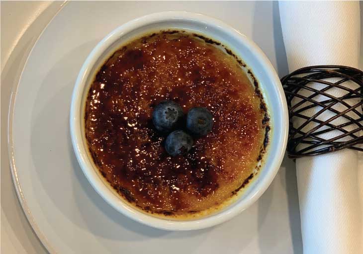 Sweet Crème Brûlée with hard sugar top lays on a white plate with napkin.