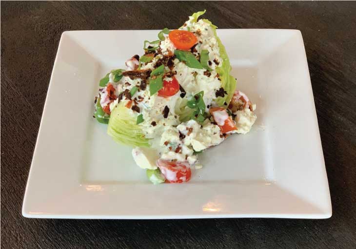 Prepared Wedge Salad with Gorgonzola dressing sits on a white plate.