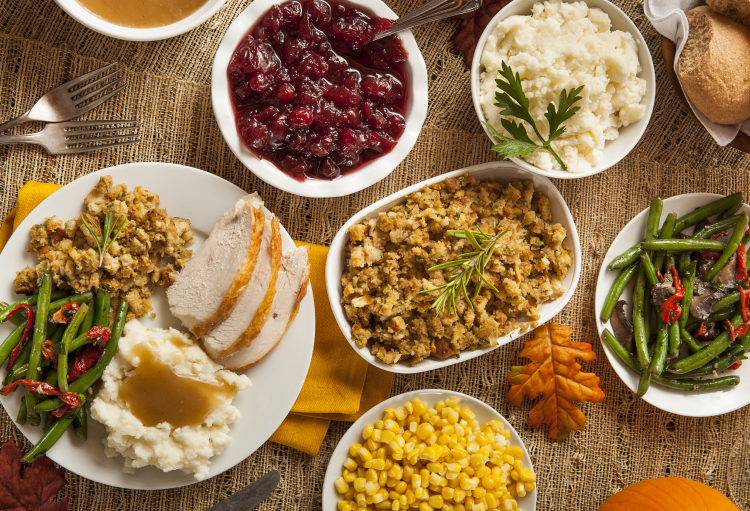 Spread of Thanksgiving dishes like turkey, mashed potatoes, stuffing, green beans, cranberry and corn on table.