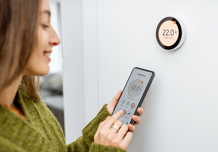 Young brunette woman in a smart home uses a phone app to change temperature settings on her nest thermostat.